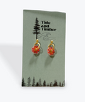 Flower-shaped earrings on a Tide and Timber branded card.