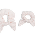 Two light pink scrunchies with bow details on a white background