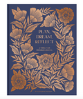 A hardcover journal with a navy blue cover decorated with metallic gold botanical illustrations and the title 'PLAN, DREAM, REFLECT' in gold lettering.