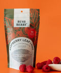 Packaging of Bush Berry Raspberry Leaf & Mint tea with raspberries on an orange background