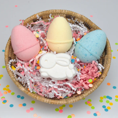Colorful bath bombs in a wicker basket with confetti on a light gray background