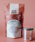 Bush Berry Rooibos Chai packaging with a clear container on a pink background