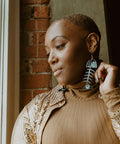 A person  looks out a window while wearing black acrylic Medium Salmon Ghost earrings from Copper Canoe Woman.