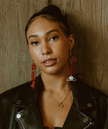 A model wearing red Medium Salmon Ghost earrings from Copper Canoe Woman stares into camera.