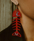 A closeup of a model wearing the Medium Salmon Ghost earrings from Copper Canoe Woman in a red acrylic.