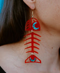 A Medium Salmon Ghost earring from Copper Canoe Woman in red acrylic worn by a model in closeup.