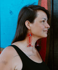 Model standing in profile wears a pair of Medium Salmon Ghost earrings in red acrylic from Copper Canoe Woman.