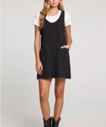 Woman wearing a black pinafore dress over a white shirt on a light gray background