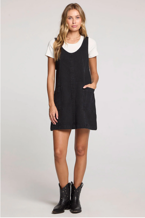 Woman wearing a black pinafore dress over a white shirt on a light gray background