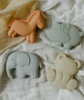 Four silicone animal-shaped teether toys on a white fabric background