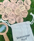 Wooden nature scavenger hunt cards with a magnifying glass and drawstring bag on grass.
