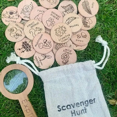 Wooden nature scavenger hunt cards with a magnifying glass and drawstring bag on grass.