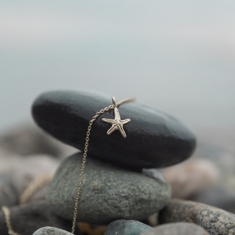 Starfish pendant necklace on a stone with a blurred natural background