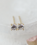 Pair of gold stud earrings with clear gemstones on a light background