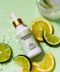 Skincare dropper bottle with 'Sukin' branding surrounded by lime and lemon slices on a green background