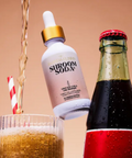 Siroom Soda bottle being poured into a glass with a straw, against a brown background