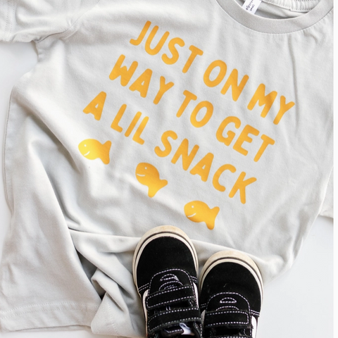 White t-shirt with yellow text and fish graphics, paired with black sneakers on a white background.