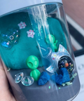 Clear container with decorative items including a green alien figure, blue creature, and space-themed decorations.