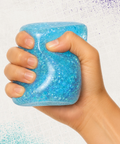 Hand squeezing a blue glitter Sugar Cube squishy toy