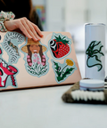 Person holding a laptop with stickers, surrounded by various items on a table.