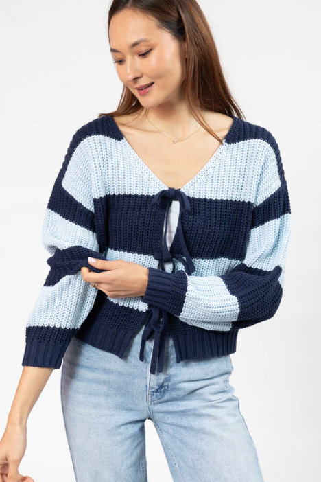 Woman wearing a blue and white striped sweater with a tie detail on a white background