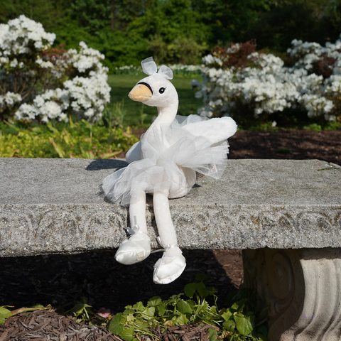 White plush duck toy sitting on a stone bench with a garden background
