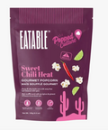 A stand-up pouch of Eatable Popped Culture Sweet Chili Heat gourmet popcorn on a plain white background. The packaging is dark purple with pink and white text and graphics, including cactus silhouettes, lime wedges, a red chili pepper, and popcorn illustrations.