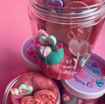 Jar with colorful heart-shaped objects on a pink background