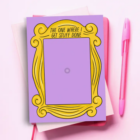 Notepad with yellow frame design and text on purple background, pink pen on side