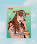 Card with illustration of a woman in a glamorous outfit and text 'The Life of a Birthday Girl' on a light blue background.