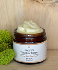 A jar of 'Nature's Timeless Tallow' moisturizer on a wooden surface, with a label that includes the product name and the claim of being 'Toxin Free'. The jar is accompanied by a small amount of product visible on a green moss pad.