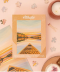 Villager puzzle box with a scenic design on a pink background with puzzle pieces and a candle.