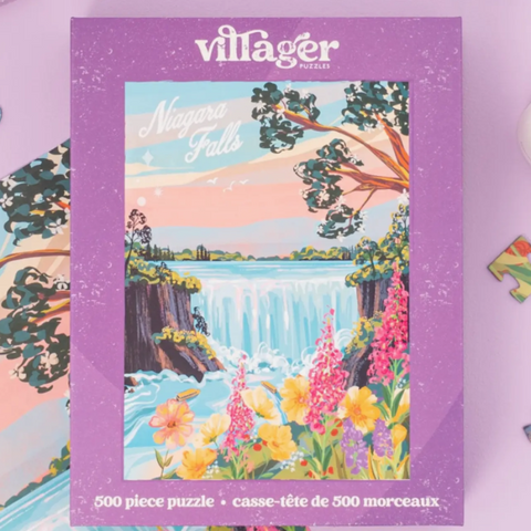 A Villager Puzzles 'Niagara Falls' 500-piece jigsaw puzzle box, featuring a colorful illustration of the waterfall surrounded by flowers and trees, set against a light purple background.