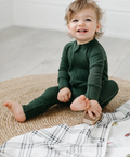 Child wearing a green onesie sitting on a textured surface with a blanket.