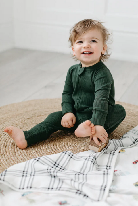 Child wearing a green onesie sitting on a textured surface with a blanket.