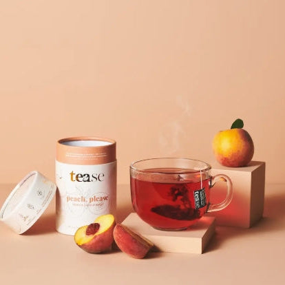 Tea canister labeled 'tease' with a glass of tea, peach slices, and an orange on a beige background.