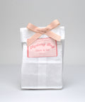White mystery bag with a pink bow and label on a gray background