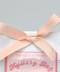 White bag with pink ribbon and label reading 'Mystery Bag Sticker Stash' on a gray background