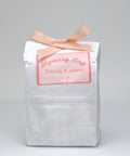 White paper bag with a pink ribbon and label on a gray background