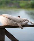 Plush whale toy on a wooden railing with a blurred natural background