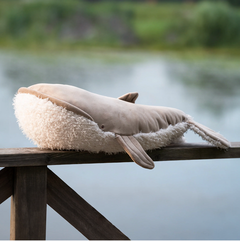 Plush whale toy on a wooden railing with a blurred natural background