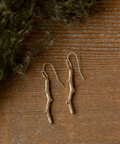 Bronze branch-shaped earrings on a wooden surface with greenery.