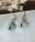 Gold earrings with light blue stones on a speckled surface