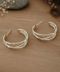 Pair of silver hoop earrings on a wooden surface with dried flowers in the background.