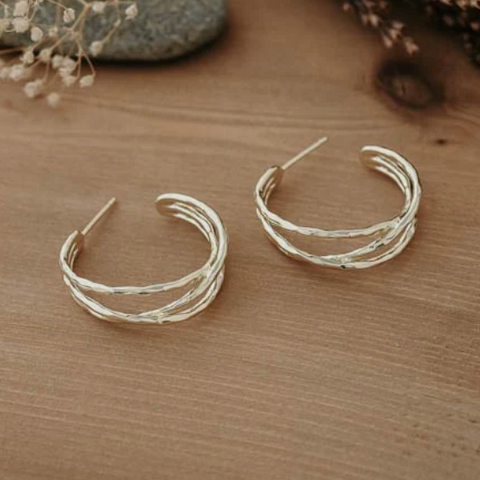 Pair of silver hoop earrings on a wooden surface with dried flowers in the background.