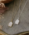 Two necklaces with pendant stones on a textured surface with dried flowers.