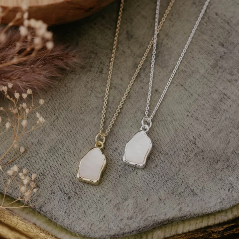 Two necklaces with pendant stones on a textured surface with dried flowers.
