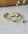 Gold heart-shaped ring with a white stone on a textured fabric background with small flowers.