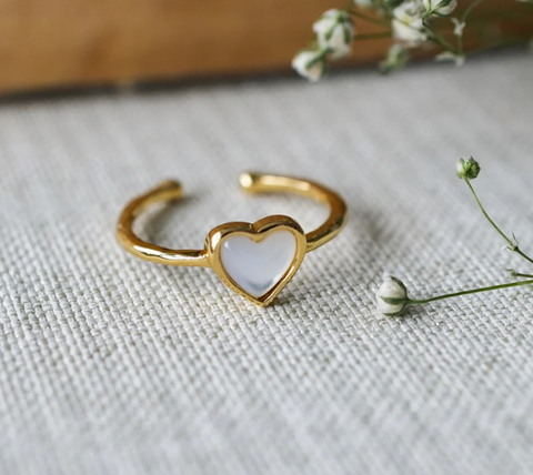 Gold heart-shaped ring with a white stone on a textured fabric background with small flowers.