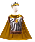 A children's royal costume set displayed on a white mannequin against a white background, featuring a metallic silver cape with brown faux-fur trim, a golden-yellow velvet hood, a matching crown, and a printed royal crest on the back of the cape.